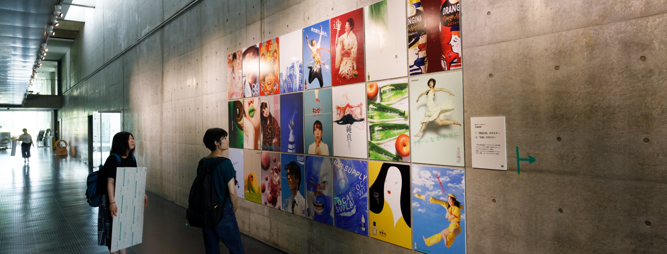 廊下の壁に展示された作品とそれを見る学生